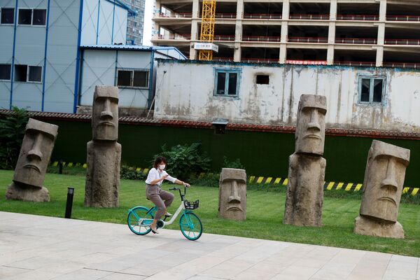 Девушка на велосипеде перед копиями Моаи в деловом районе Пекина  - Sputnik Абхазия