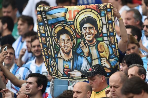 Болельщик Аргентины держит изображение нападающего Аргентины Лионеля Месси и бывшего футболиста Диего Марадоны в образе Святых перед футбольным матчем на стадионе Бейра-Рио в Порту-Алегри - Sputnik Абхазия