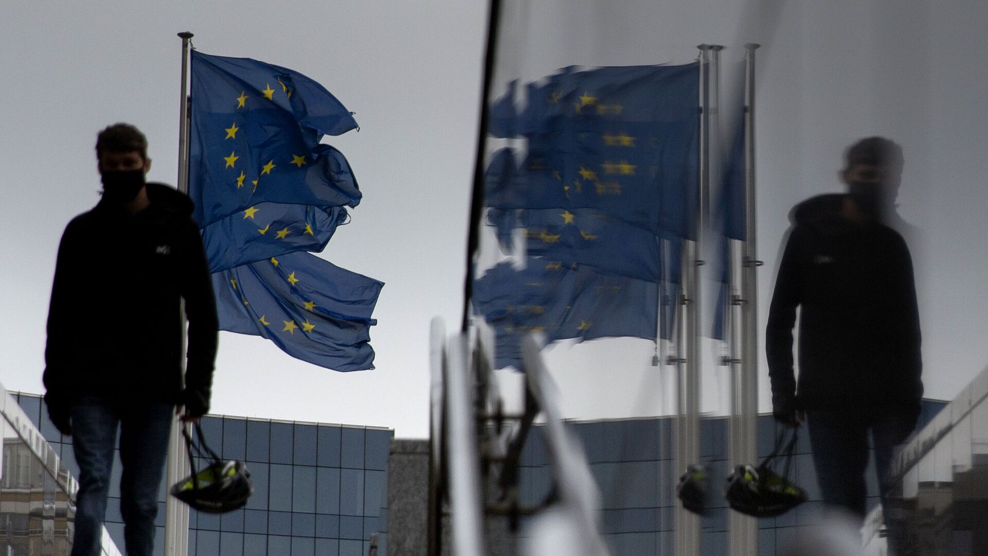 Мужчина идет мимо флагов ЕС у штаб-квартиры ЕС в Брюсселе - Sputnik Абхазия, 1920, 05.01.2022