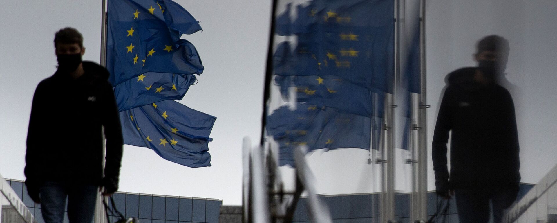 Мужчина идет мимо флагов ЕС у штаб-квартиры ЕС в Брюсселе - Sputnik Абхазия, 1920, 10.12.2020