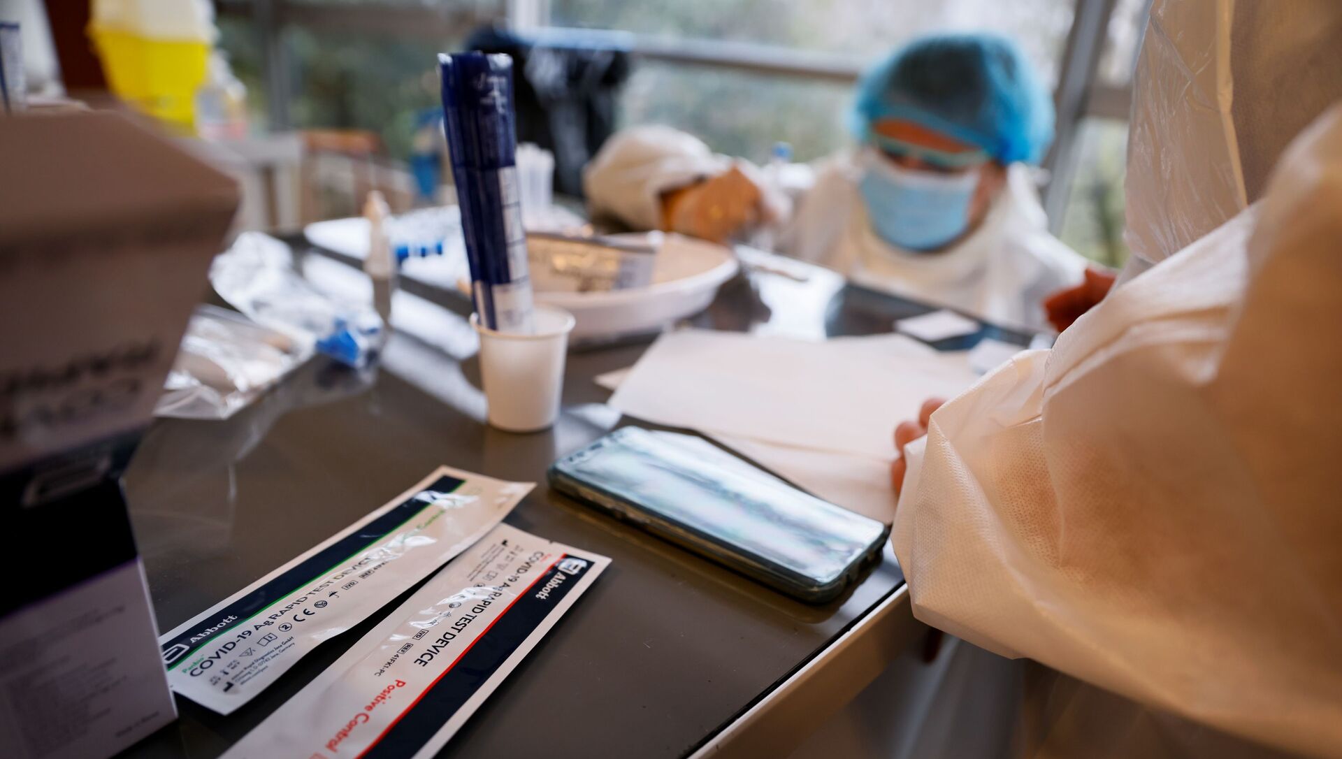 Наборы для тестирования антигена лежат на столе, пока медицинский работник проводит тест во время операции по массовому скринингу на Covid-19 - Sputnik Абхазия, 1920, 13.07.2021