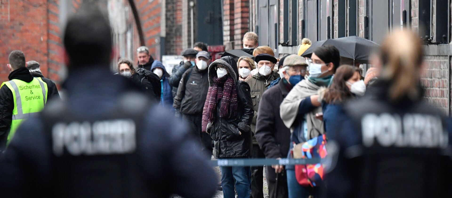 Полиция ждет, пока люди в масках выстраиваются в очередь, чтобы получить доступ к центру вакцинации на «Арене» в берлинском районе Трептов  - Sputnik Абхазия, 1920, 29.01.2021