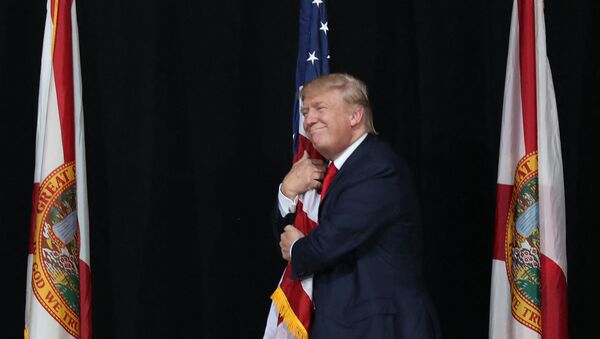 Тампа, Флорида - 24 октября: Кандидат в президенты от республиканцев Дональд Трамп обнимает американский флаг, когда он прибывает на митинг кампании в амфитеатре кредитного союза MidFlorida 24 октября 2016 года в Тампе, Флорида. До президентских выборов осталось 14 дней. Джо Рэдл / Getty Images / AFP (Фото Джо Рэдла - Sputnik Абхазия