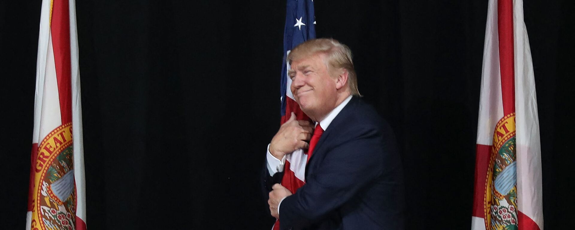 Тампа, Флорида - 24 октября: Кандидат в президенты от республиканцев Дональд Трамп обнимает американский флаг, когда он прибывает на митинг кампании в амфитеатре кредитного союза MidFlorida 24 октября 2016 года в Тампе, Флорида. До президентских выборов осталось 14 дней. Джо Рэдл / Getty Images / AFP (Фото Джо Рэдла - Sputnik Абхазия, 1920, 12.11.2022