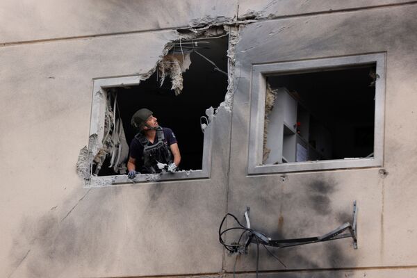 Эксперт по обезвреживанию бомб израильской полиции смотрит из окна жилого дома, который был поврежден после попадания в него ракеты, запущенной из сектора Газа, в Ашкелоне - Sputnik Абхазия