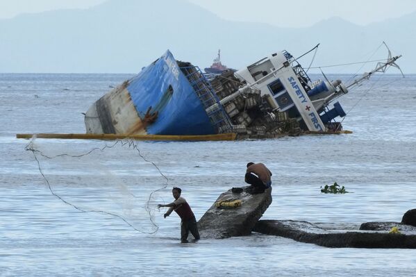 Рыбак бросает сеть рядом с наполовину затопленным судном в заливе Манила, Филиппины. - Sputnik Абхазия