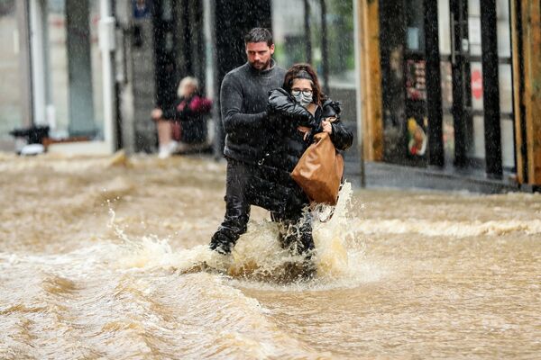 Мужчина помогает женщине пройтись по затопленной улице в городе Спа, Бельгия - Sputnik Абхазия