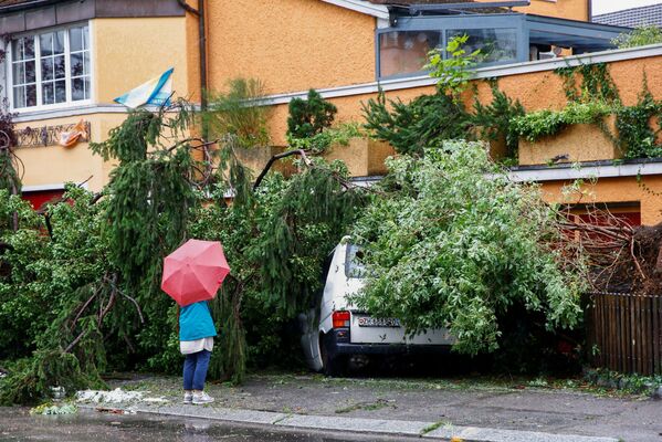 Женщина стоит перед фургоном, поврежденным упавшим деревом во время грозы и проливного дождя в Цюрихе, Швейцария. - Sputnik Абхазия