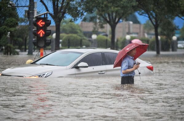 Мужчина у затопленной в результате проливных дождей машины после проливных дождей в Чжэнчжоу в центральной провинции Китая Хэнань. - Sputnik Абхазия