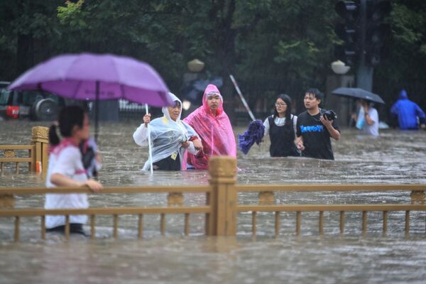 Люди пробирающиеся через паводковые воды по улице после проливных дождей в Чжэнчжоу в центральной провинции Китая Хэнань. - Sputnik Абхазия