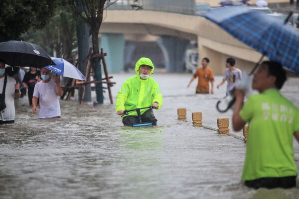 Мужчина едет на велосипеде через паводковые воды по улице после проливных дождей в Чжэнчжоу в центральной провинции Китая Хэнань. - Sputnik Абхазия