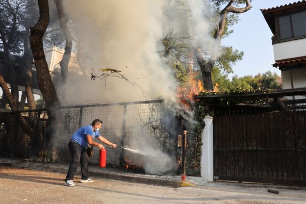 Мужчина с огнетушителем пытается тушить лесной пожар в пригороде Варимпомпи к северу от Афин. - Sputnik Абхазия