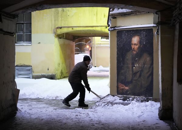 Муниципальный служащий убирает снег во дворе рядом с портретом русского писателя Федора Достоевского в центре Санкт-Петербурга после циклона, принесшего первый снегопад в этом году - Sputnik Абхазия