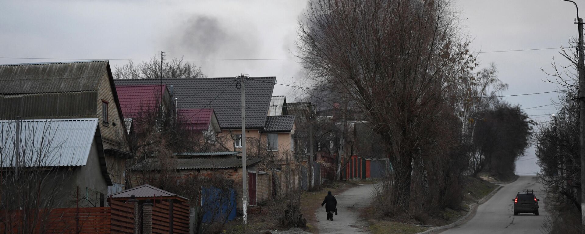 Местный житель идет по улице, когда поднимается дым возле города Хостомель и аэропорта Антонов, на северо-западе Киева - Sputnik Абхазия, 1920, 25.02.2022