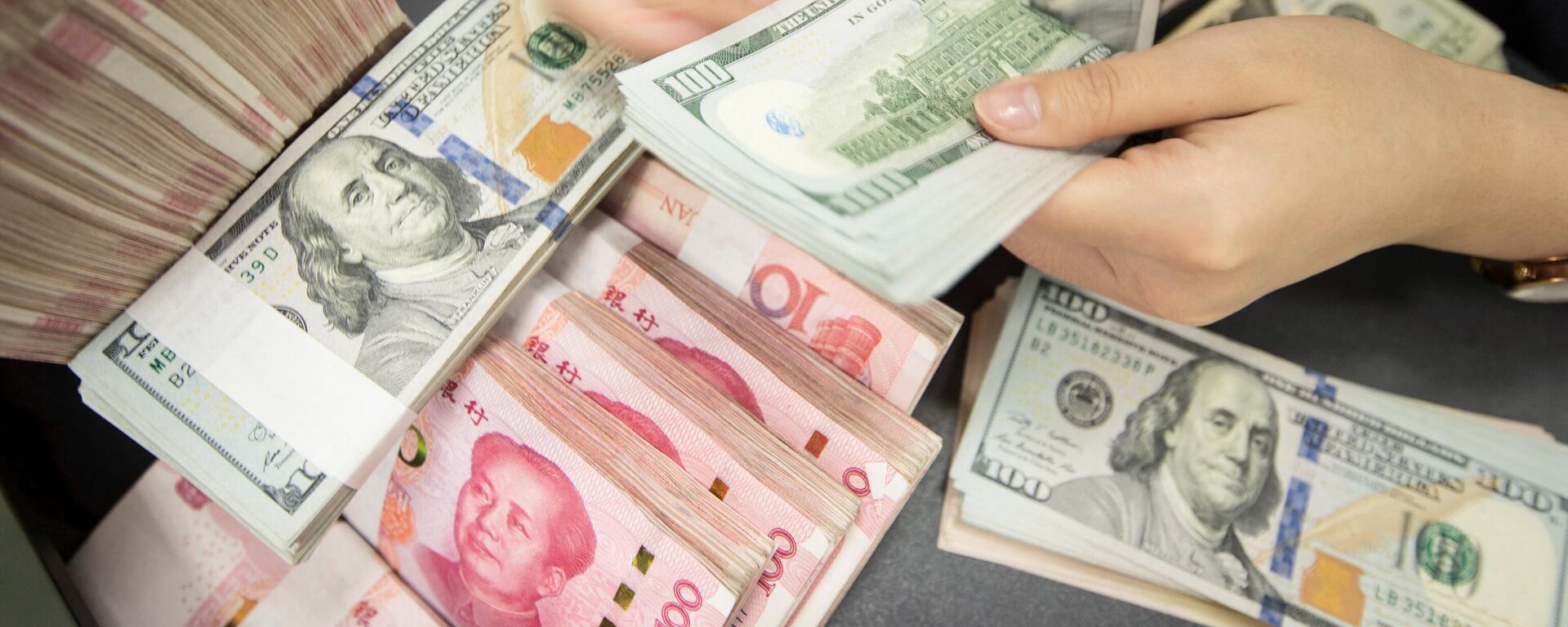 Сотрудник китайского банка пересчитывает банкноты в 100 юаней и купюры в долларах США - Sputnik Абхазия, 1920, 04.04.2022