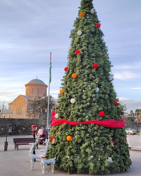 Елку в Пицунде украсили белыми, оранжевыми и красными шарами, а у ее подножья красуются новогодние олени. - Sputnik Абхазия