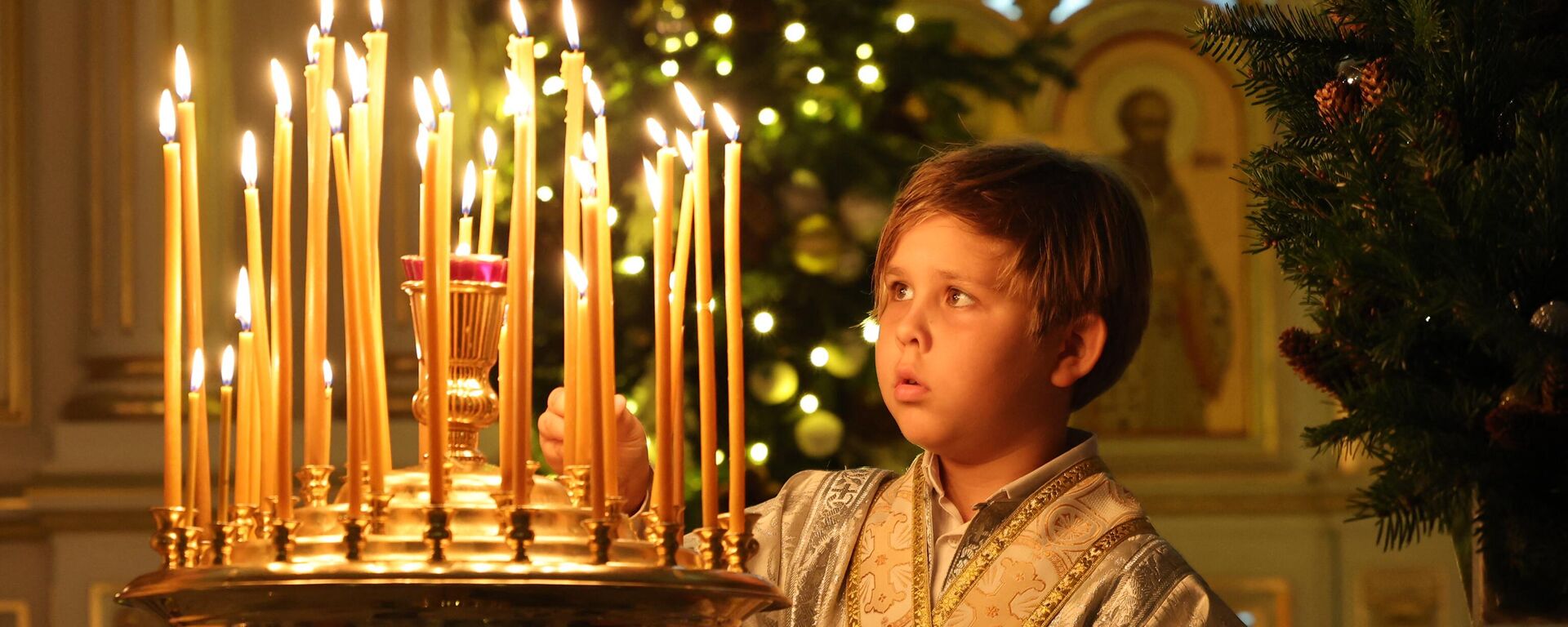 Мальчик зажигает свечу во время празднования православного Рождества в Русской православной церкви в Шардже - Sputnik Абхазия, 1920, 07.01.2023