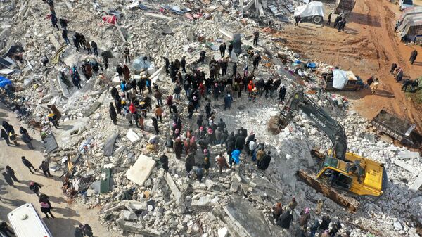 На этом снимке с воздуха показаны жители, ищущие жертв и выживших среди обломков разрушенных зданий после землетрясения в деревне Бесния недалеко от города Харим в удерживаемой повстанцами северо-западной сирийской провинции Идлиб на границе с Турцией, 6 февраля 2022 года. - Sputnik Аҧсны