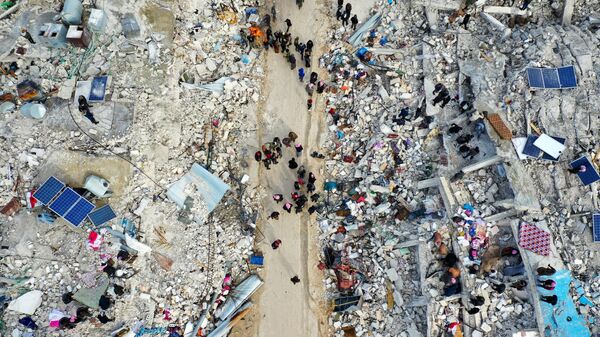 На этом снимке с воздуха показаны жители, ищущие жертв и выживших среди обломков разрушенных зданий после землетрясения в деревне Бесния недалеко от города Харим в удерживаемой повстанцами северо-западной сирийской провинции Идлиб на границе с Турцией, 6 февраля 2022 года. - Sputnik Аҧсны