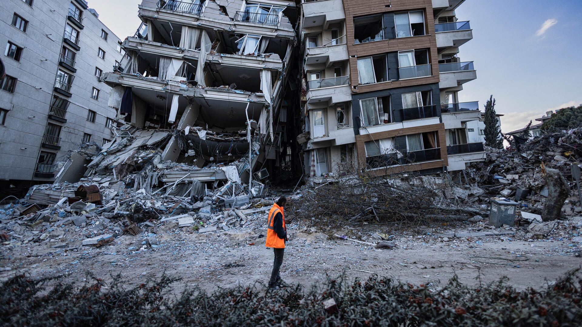 Спасатель проходит мимо частично разрушенных в результате землетрясений зданий в городе Антакья, Турция - Sputnik Аҧсны, 1920, 20.03.2023