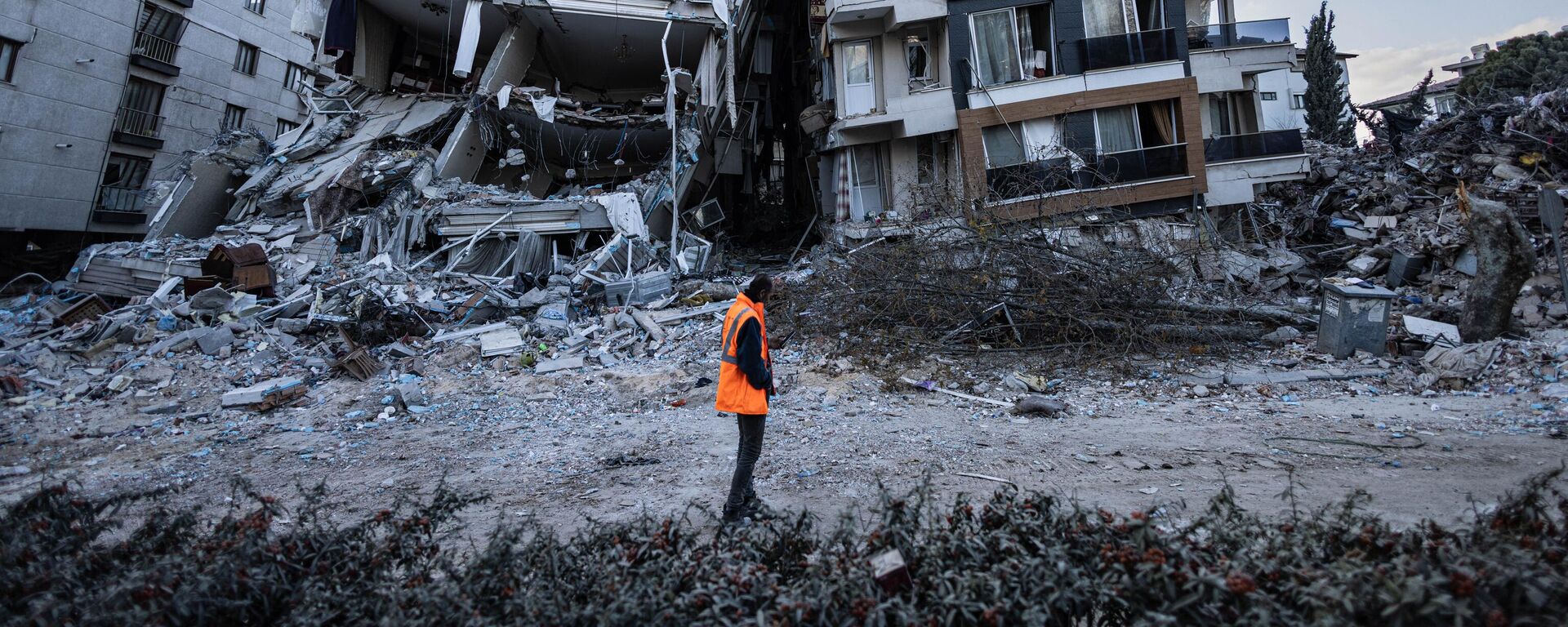 Спасатель проходит мимо частично разрушенных в результате землетрясений зданий в городе Антакья, Турция - Sputnik Абхазия, 1920, 10.03.2023