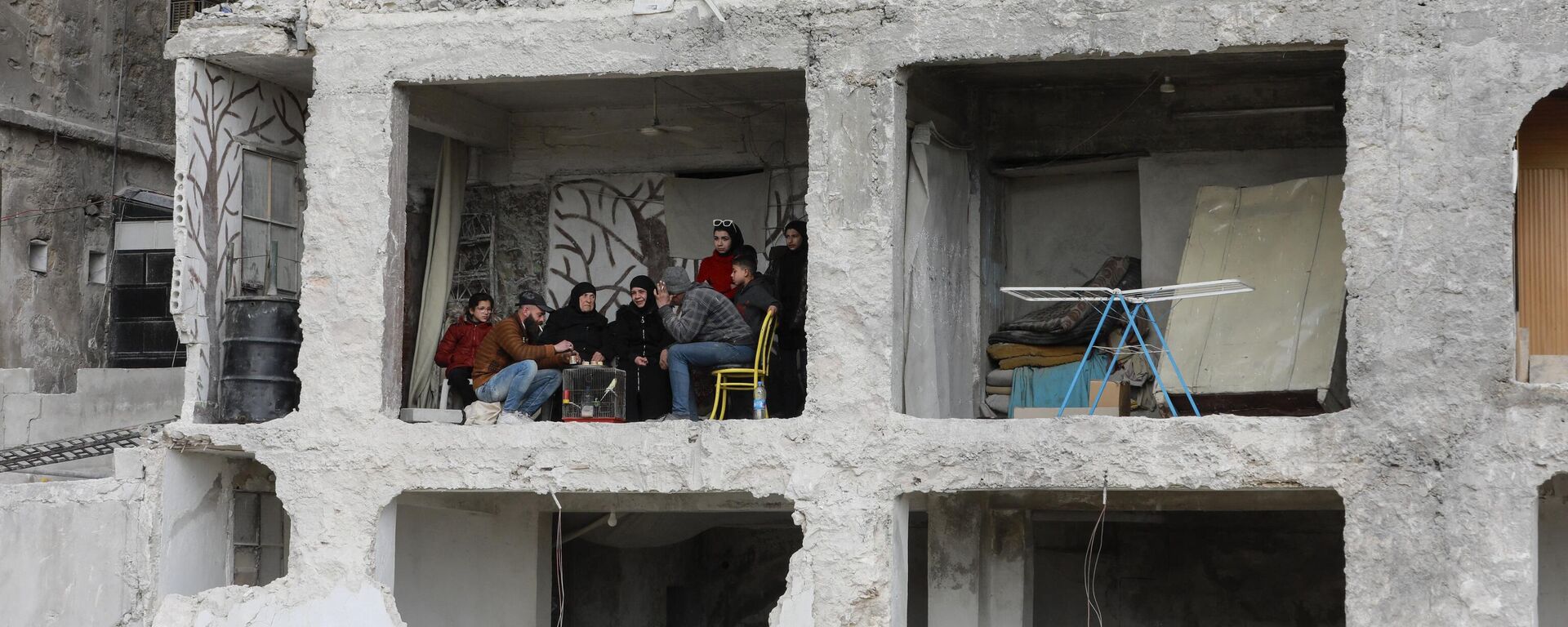 Семья за столом в здании, пострадавшем в результате землетрясения силой 7,8 балла, в районе Аль-Машарка города Алеппо, Сирия - Sputnik Абхазия, 1920, 20.03.2023