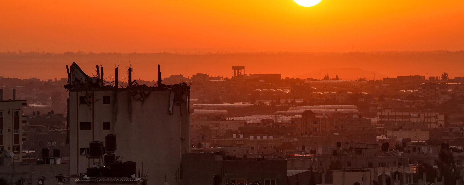 Солнце поднимается из-за поврежденного здания над горизонтом Хан-Юниса на юге сектора Газа - Sputnik Абхазия, 1920, 24.10.2023