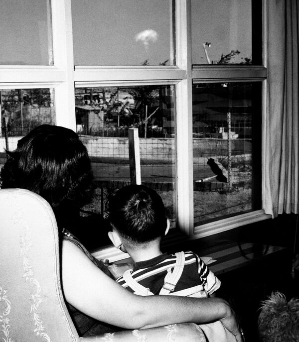 Миссис Жаклин Бак с сыном наблюдают из гостиной в Лас-Вегасе за грибовидным облаком ядерного взрыва 8 мая 1953 года на полигоне в Неваде, в 75 милях от дома. Вспышка показала, что взрыв был одним из крупнейших весенней серии испытаний. (Фото: Комиссия по атомной энергии США через AP) - Sputnik Абхазия