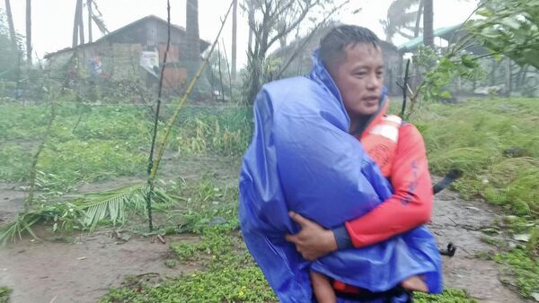 Спасатель эвакуирует ребенка в безопасное место, поскольку супертайфун Рагаса обрушился на Санта-Ану, провинция Кагаян, северные Филиппины, 22 сентября 2025 года - Sputnik Абхазия