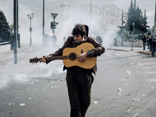 На фотографии Аггелоса Бараи молодой уличный музыкант по имени Алекс играет на гитаре возле здания греческого парламента в центре Афин, где прошли столкновения между полицией и демонстрантами На фотографии Аггелоса Бараи молодой уличный музыкант по имени Алекс играет на гитаре возле здания греческого парламента в центре Афин, где прошли столкновения между полицией и демонстрантами - Sputnik Абхазия