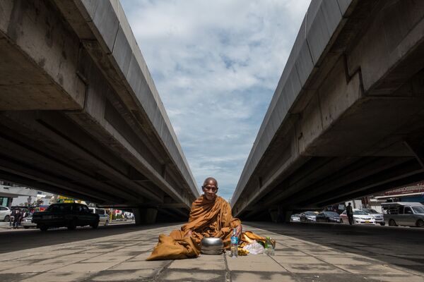 Буддийский монах сидит на земле между двумя транспортными эстакадами, и ждет милостыни. Северный Бангкок - Sputnik Абхазия