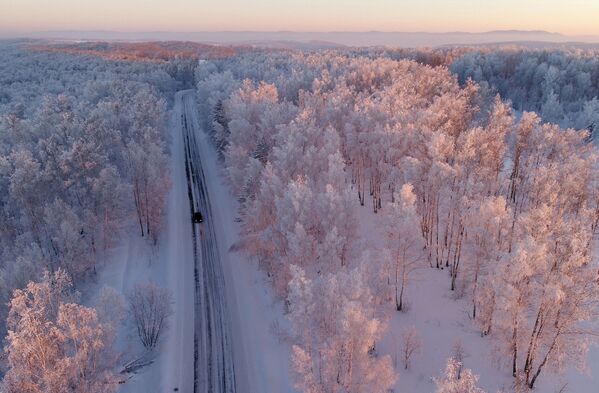 Машина едет по трассе вдоль заснеженного леса на закате, Красноярский край - Sputnik Абхазия