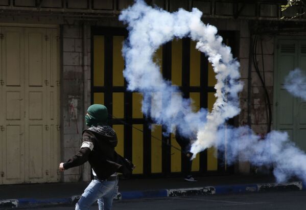 Палестинский демонстрант бросает газовую шашку в израильских солдат во время столкновений на Западном берегу реки Иордан - Sputnik Абхазия