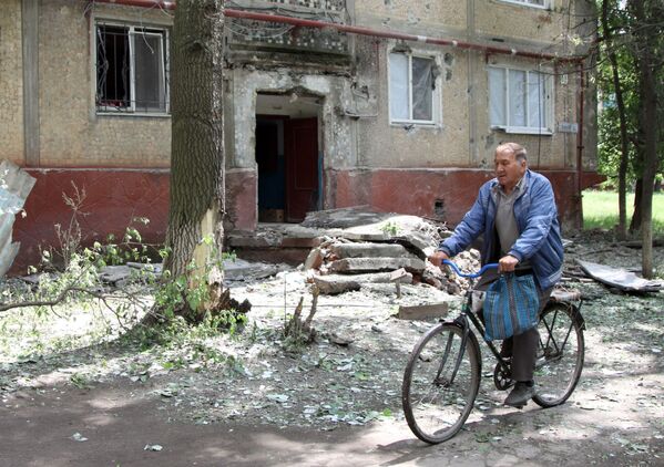 Мужчина едет на велосипеде во дворе жилого дома, пострадавшего в результате обстрела, в поселке Горловка Донецкой области - Sputnik Абхазия