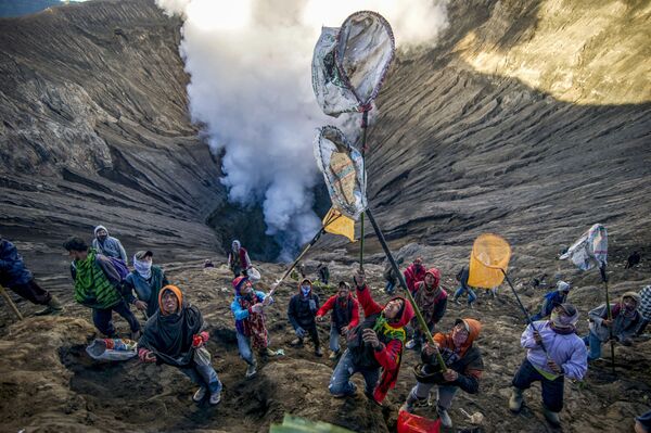 Люди готовятся ловить пожертвования, бросаемые членами племени тенгеров в кратер вулкана Бромо в Индонезии в рамках индуистского фестиваля Yadnya Kasada - Sputnik Абхазия