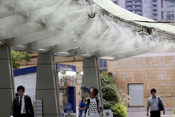 Люди под охлаждающим устройством во время жары в Токио - Sputnik Абхазия