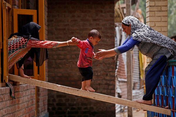 Женщины помогают ребенку перебраться на соседний дом по доске во время внезапных наводнений, Сринагар - Sputnik Абхазия