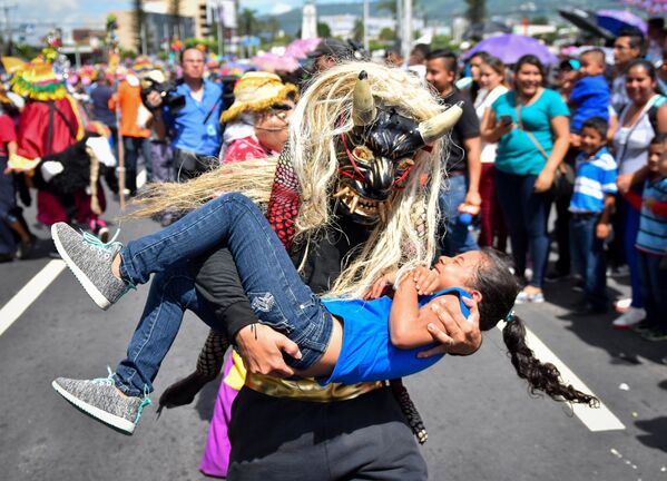 Человек в маске мифологического существа держит на руках девочку во время парада в Сан-Сальвадор - Sputnik Абхазия