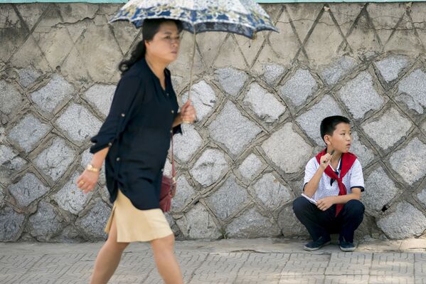 Девушка с зонтиком проходит мимо сидящего мальчика в Пхеньяне - Sputnik Абхазия