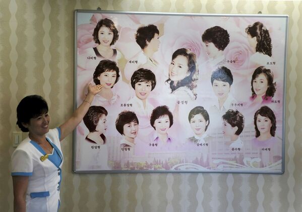 Гид показывает плакат с женскими прическами в парикмахерской Пхеньяна, Северная Корея - Sputnik Абхазия