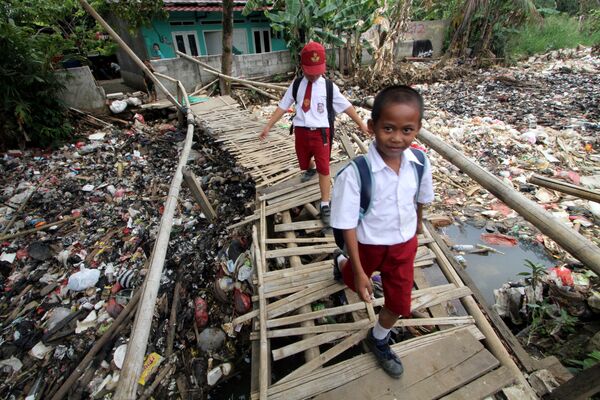Школьники идут по бамбуковому мосту над заполненным мусором рукаве реки Чиливунг в Индонезии - Sputnik Абхазия
