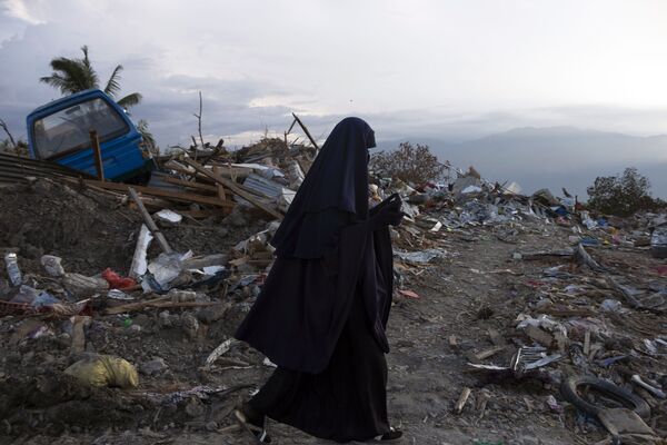 Индонезийская женщина идет мимо завалов мусора в деревне Петбо в Палу, оставшихся после землетрясения и цунами, произошедших 28 сентября - Sputnik Абхазия