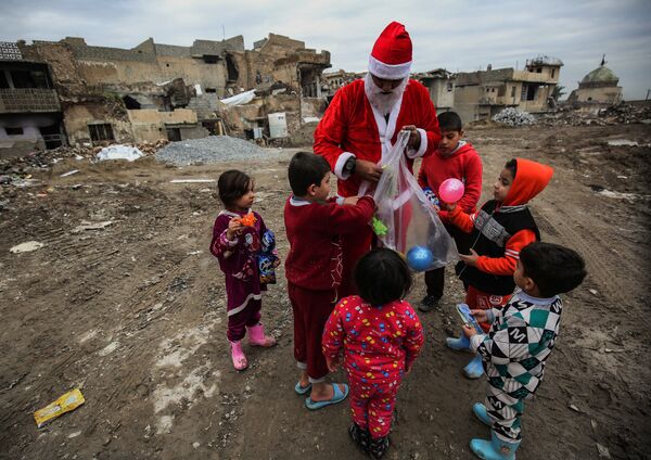 Мужчина в костюме Санта-Клауса раздает детям подарки на одной из улиц Мосула, Ирак - Sputnik Абхазия