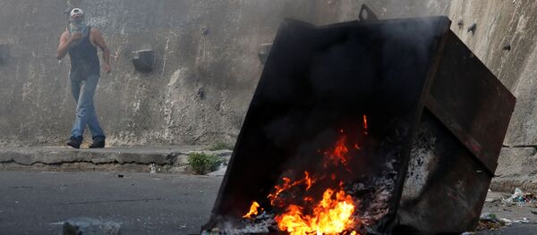 Демонстрант за горящей баррикадой во время протестов в Каракасе, Венесуэла - Sputnik Аҧсны