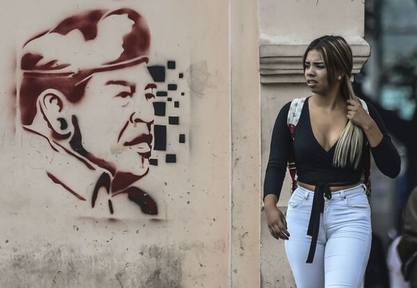 Женщина проходит мимо изображения бывшего президента Венесуэлы Уго Чавеса в Каракасе - Sputnik Абхазия