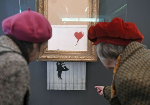 Посетители смотрят на самоуничтожившуюся после продажи на аукционе картину художника Бэнкси Девочка с воздушным шаром, которая теперь называется Любовь в мусорном баке, в Музее современного искусства в Баден-Бадене, Германия - Sputnik Абхазия