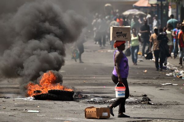 Женщина проходит мимо горящей шины на улице Порт-о-Пренсы, столицы Гаити - Sputnik Абхазия