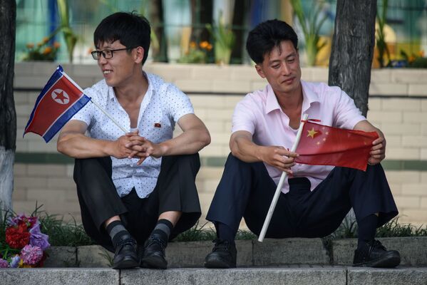 Двое мужчин с флагами Северной Кореи и Китая у площади Ким Ир Сена в Пхеньяне во время визита президента Китая Си Цзиньпина в Северную Корею - Sputnik Абхазия