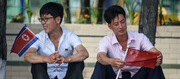 Двое мужчин с флагами Северной Кореи и Китая у площади Ким Ир Сена в Пхеньяне во время визита президента Китая Си Цзиньпина в Северную Корею Двое мужчин с флагами Северной Кореи и Китая у площади Ким Ир Сена в Пхеньяне во время визита президента Китая Си Цзиньпина в Северную Корею - Sputnik Абхазия