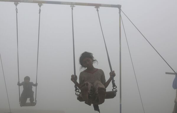 Дети катаются на качелях на детской площадке, окруженной смогом, в Лахоре - Sputnik Абхазия